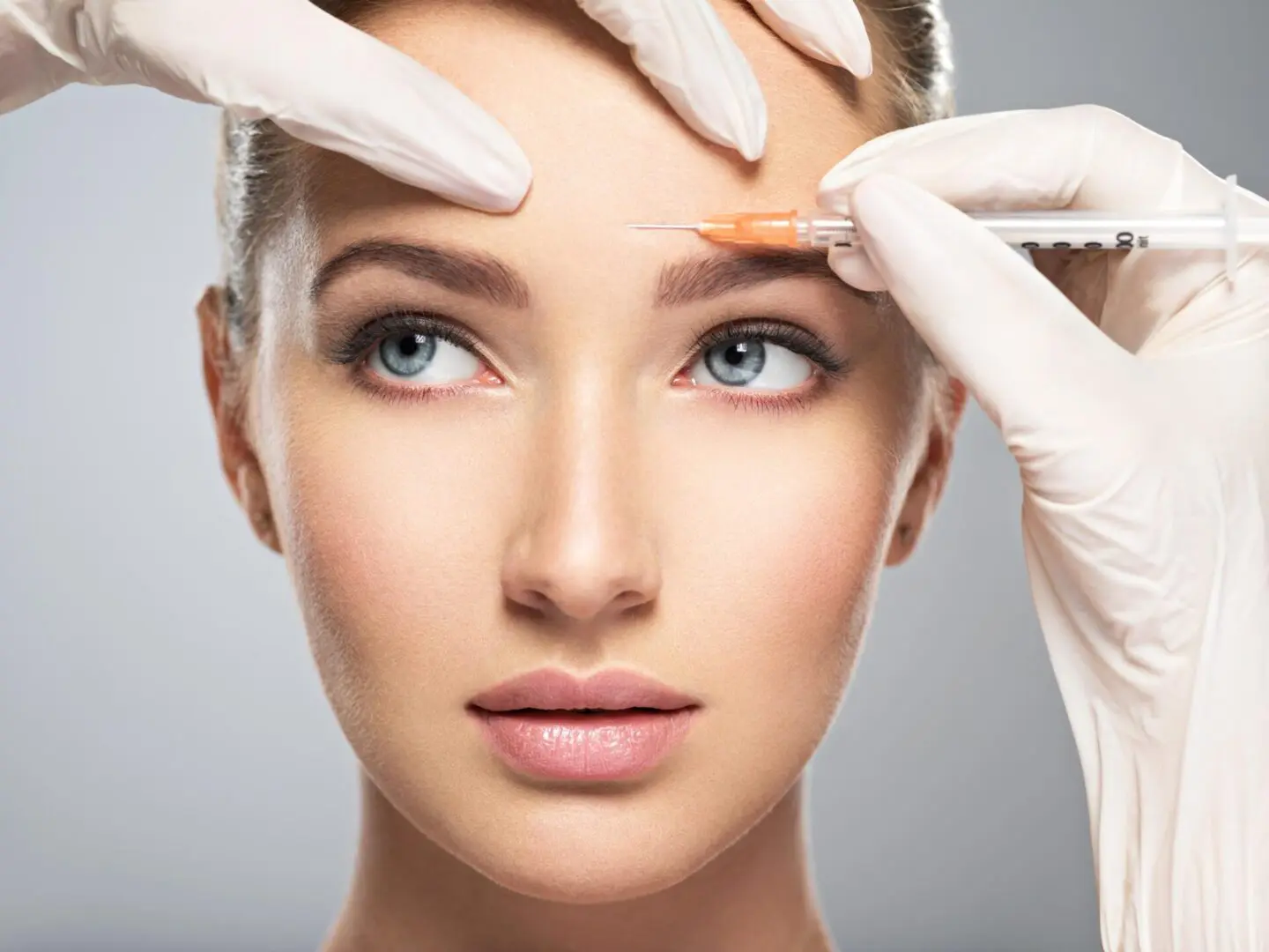 A woman getting her eyebrows waxed by two hands.